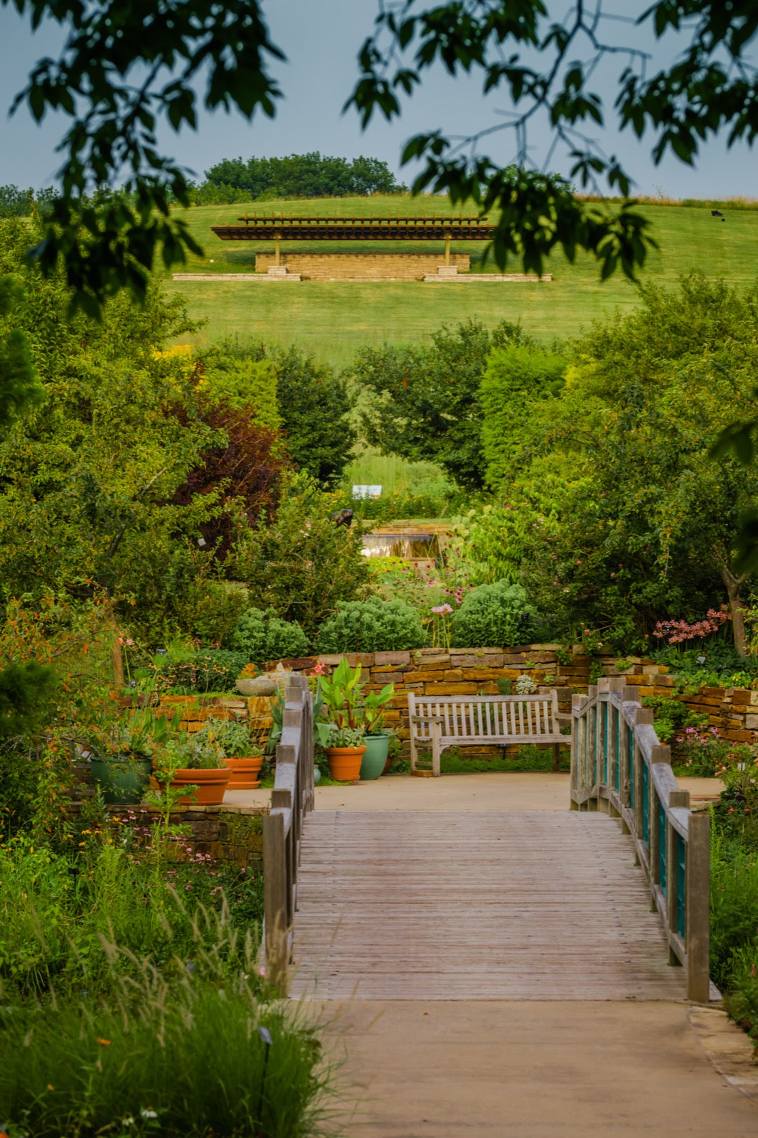 Wooden footbridge crossing to the Island Garden with lush plantings at Powell Gardens botanical garden near Kansas City Missouri